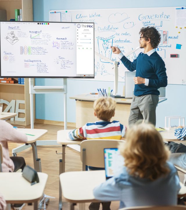 Elementary School Physics Teacher Uses Interactive Digital Whiteboard With Green Screen Mock-up Template. He Leads Lesson to Classroom full of Smart Diverse Children. Science Class with Kids Listening